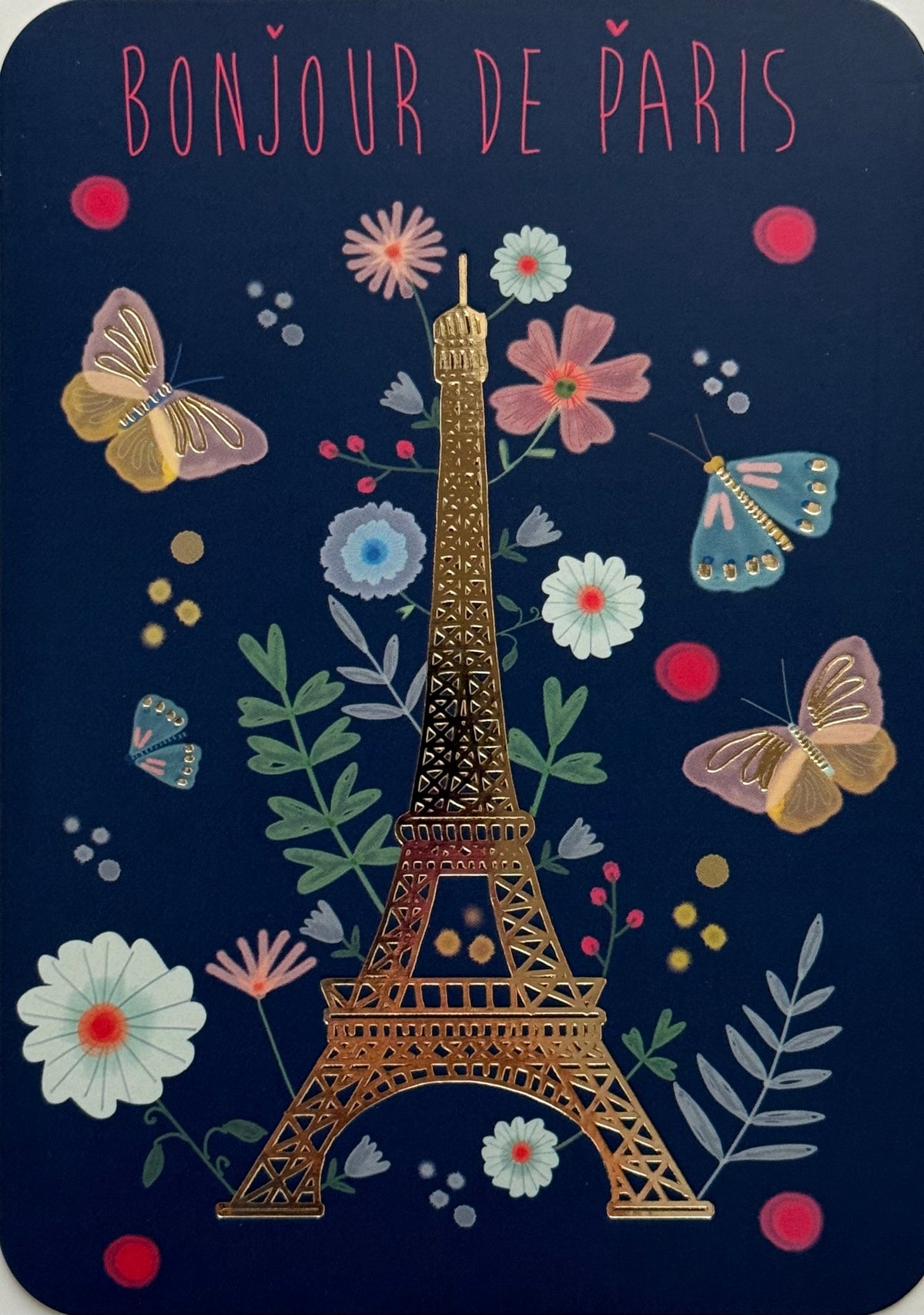 Hello from Paris Postcard by Cartes d'Art featuring the Eiffel Tower centered on a dark navy background, surrounded by illustrated flowers, butterflies, and the words “BONJOUR DE PARIS” at the top in pink.
