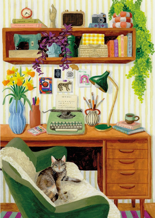 Coworking Cat Postcard by Mélanie Voituriez featuring a cozy illustrated home office scene with a green armchair holding a tabby cat, a wooden desk with a typewriter, books, flowers, shelves, and hanging greenery against striped wallpaper.