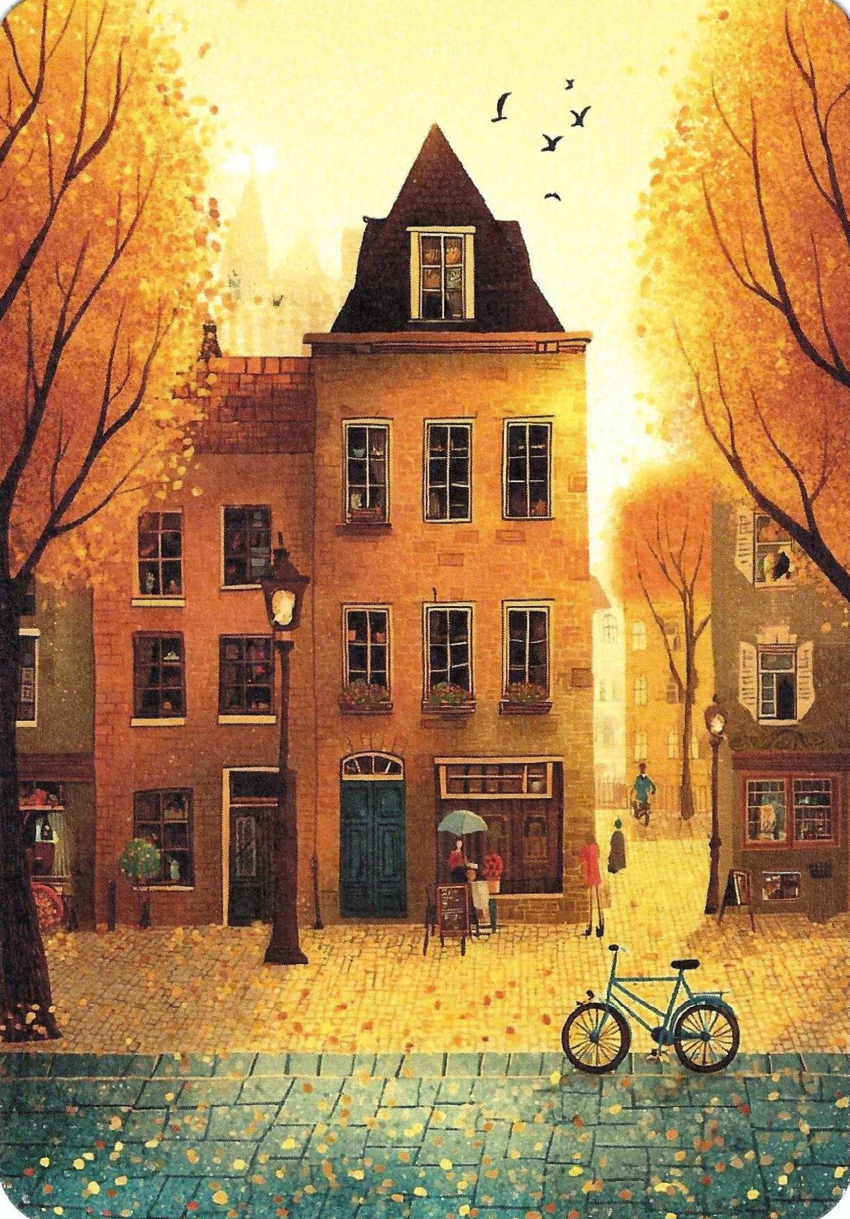 Blue Door Cafe Postcard by Fripperies - Golden Season featuring a warm-toned illustrated street scene with old brick buildings, autumn trees, a bicycle in the foreground, and a person in front of a cafe.