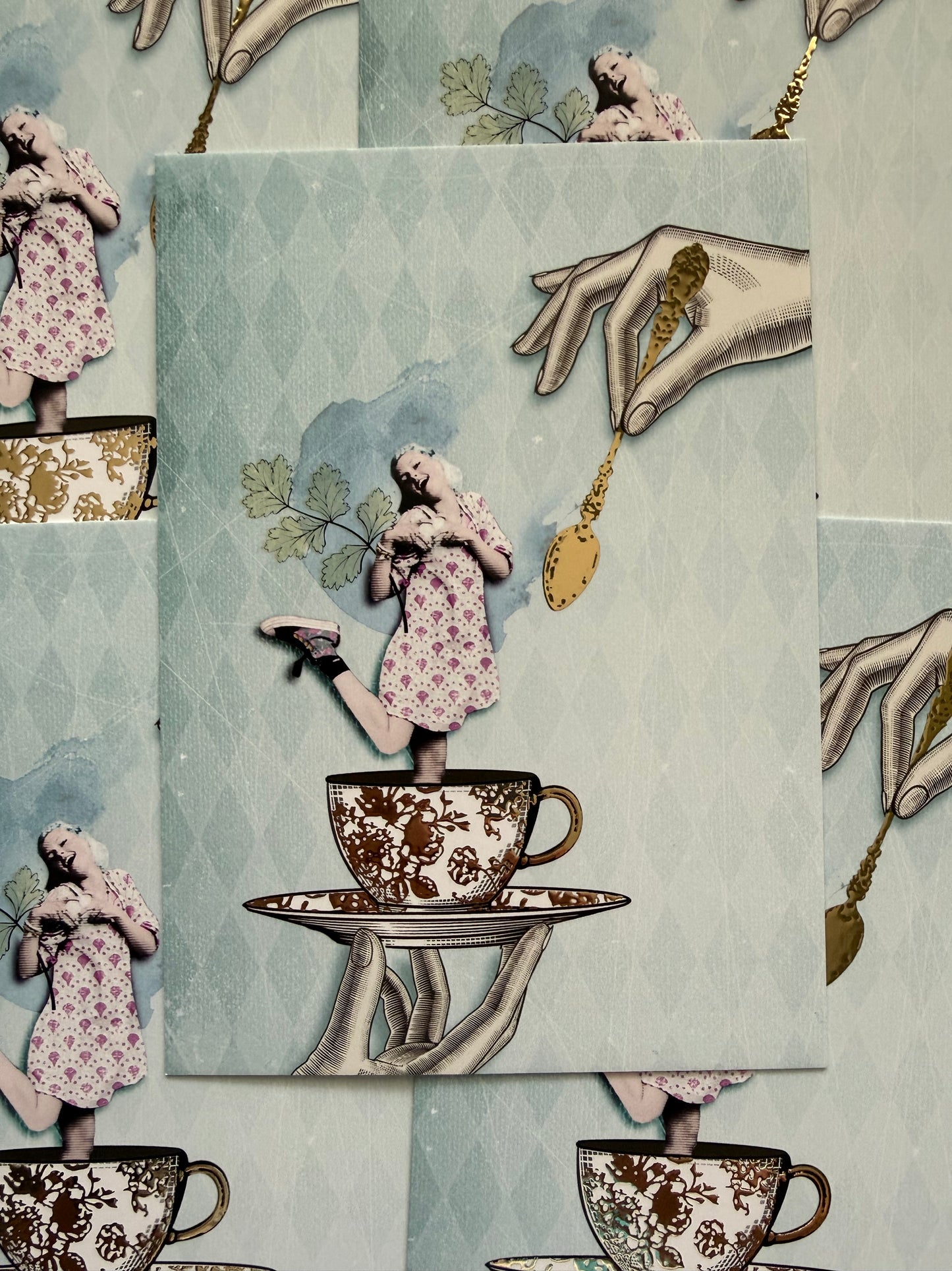 Golden Girl Postcard by La Tack for Nobis Design featuring an illustration of a girl in a dress being held in a teacup and saucer with a golden spoon above.