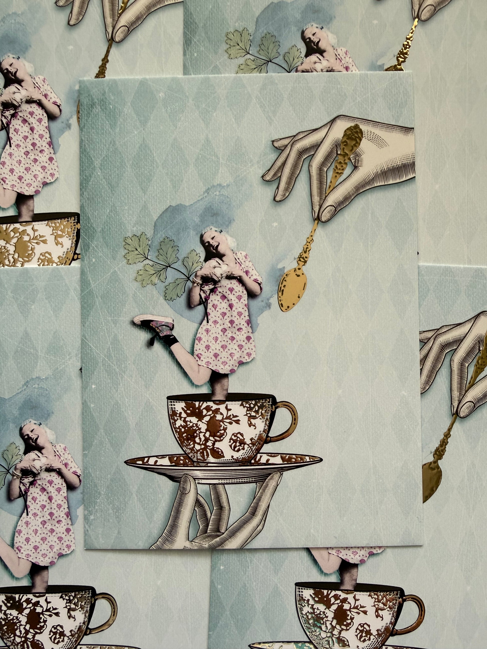 Golden Girl Postcard by La Tack for Nobis Design featuring an illustration of a girl in a dress being held in a teacup and saucer with a golden spoon above.