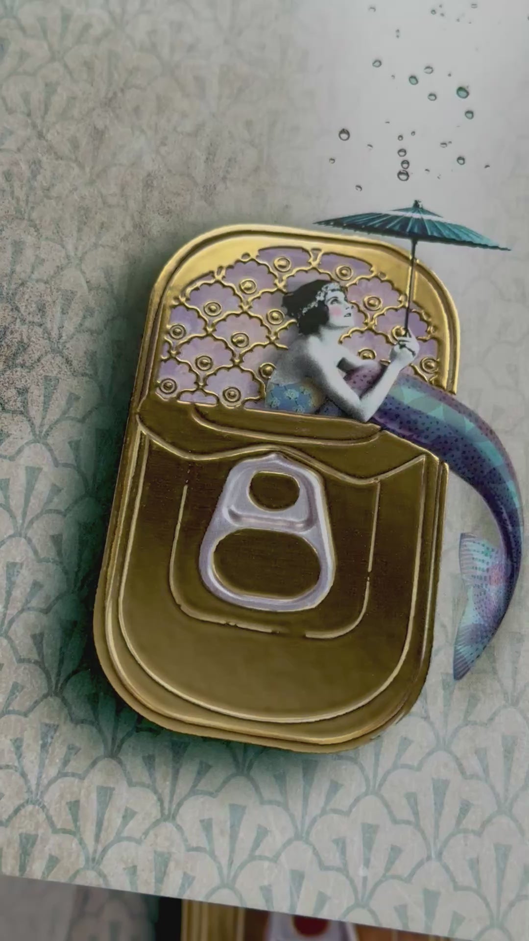 Mermaid Postcard by La Tack for Nobis Design featuring a mermaid holding an umbrella sitting in a sardine can on a decorative background. Video depicts the shiny gold foil detailing.